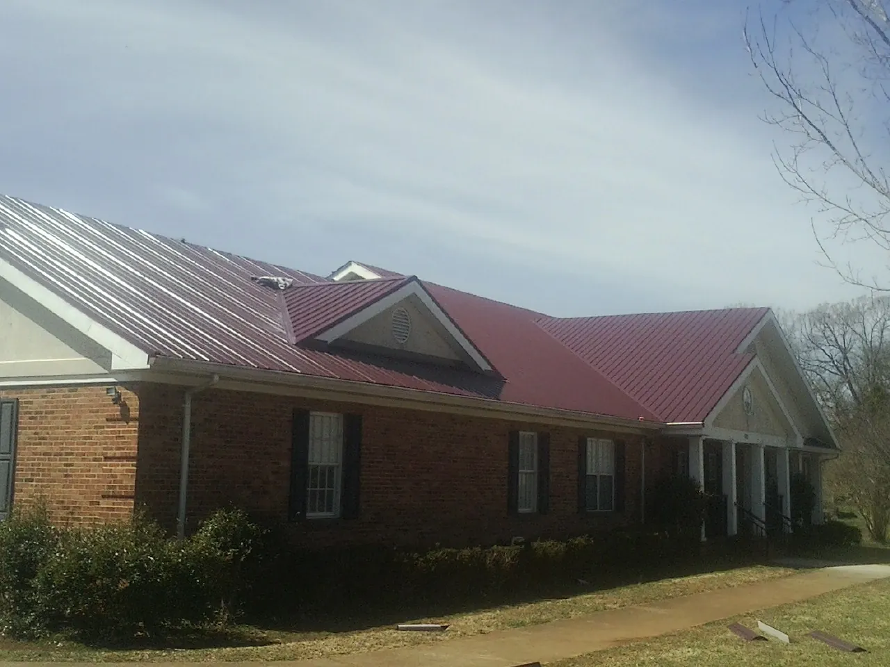 Red metal roof with gabled entries on a long brick building, from a Hail Damage Roof Repair job in Live Oak